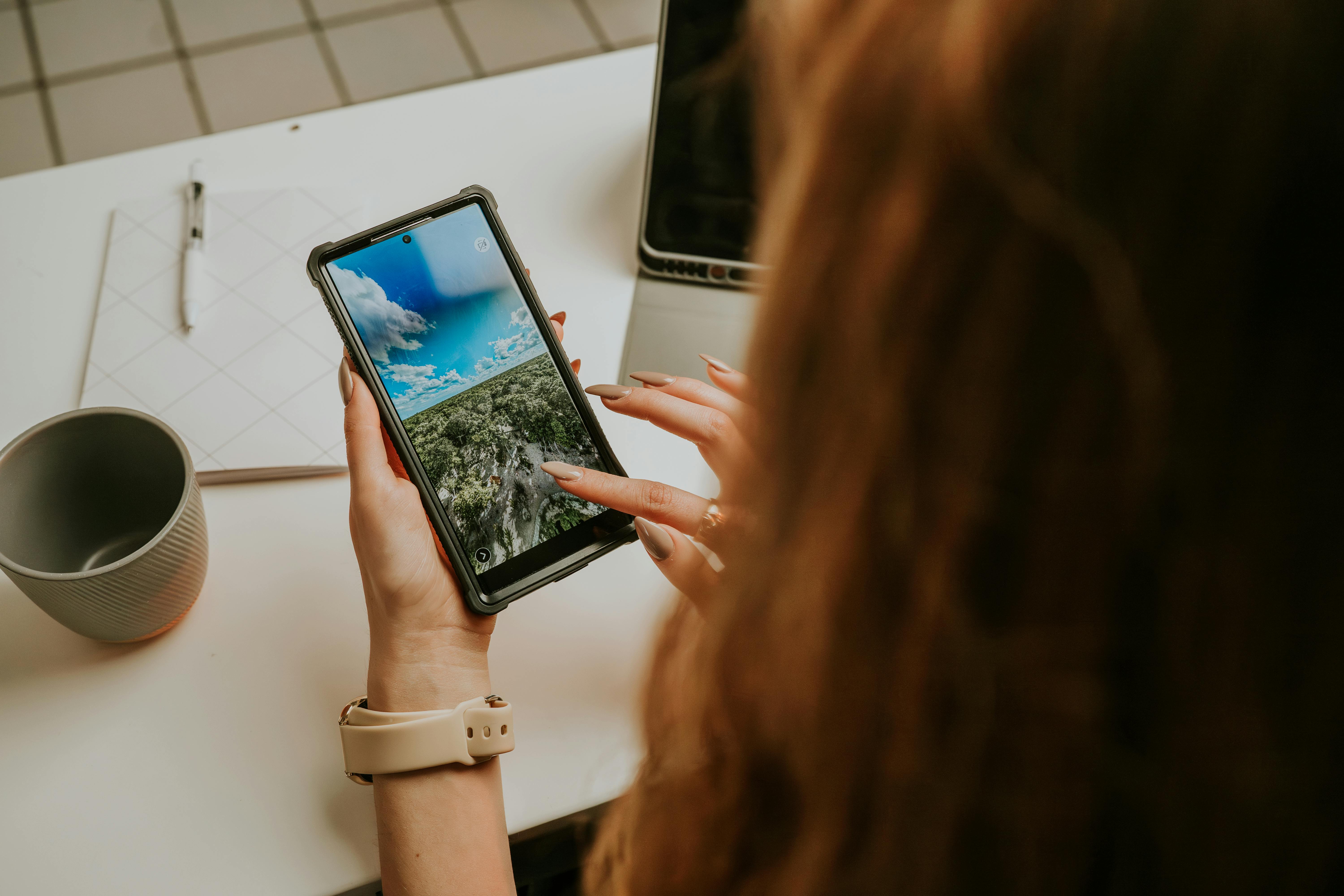 Close-up of a woman using a smartphone at a desk, indicating a modern office environment.